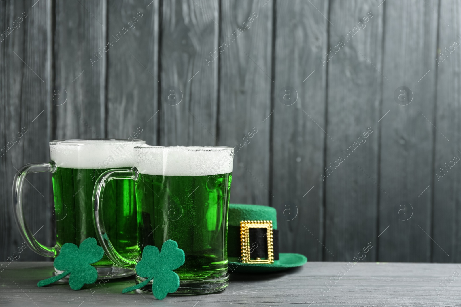 Photo of Green beer, hat and clover leaves on grey wooden table, space for text. St. Patrick's Day celebration