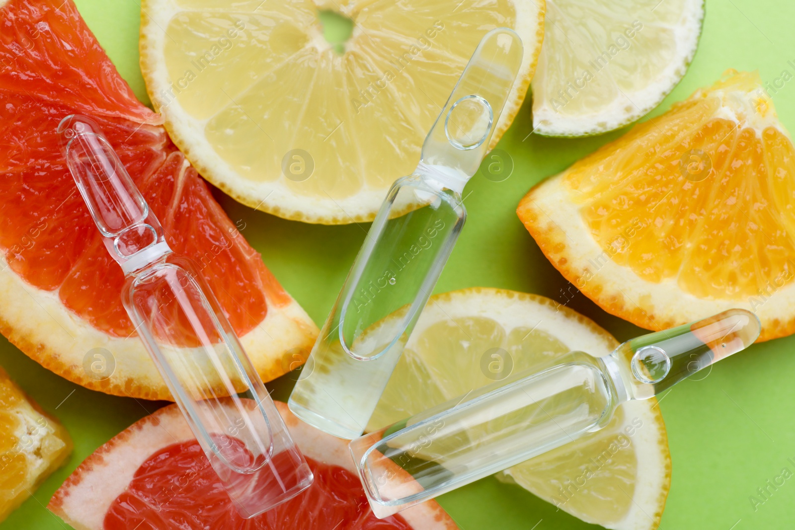 Photo of Pharmaceutical ampoules with medication and citrus fruits on green background, flat lay