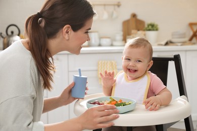 Photo of Mother feeding her cute little baby in kitchen