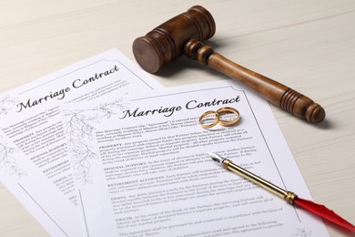 Marriage contracts, gold rings, pen and gavel on light wooden table, closeup