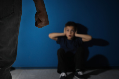 Man threatens his son on blue background, focus on hand. Domestic violence concept
