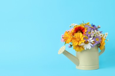 Photo of Yellow watering can with beautiful flowers on light blue background, space for text