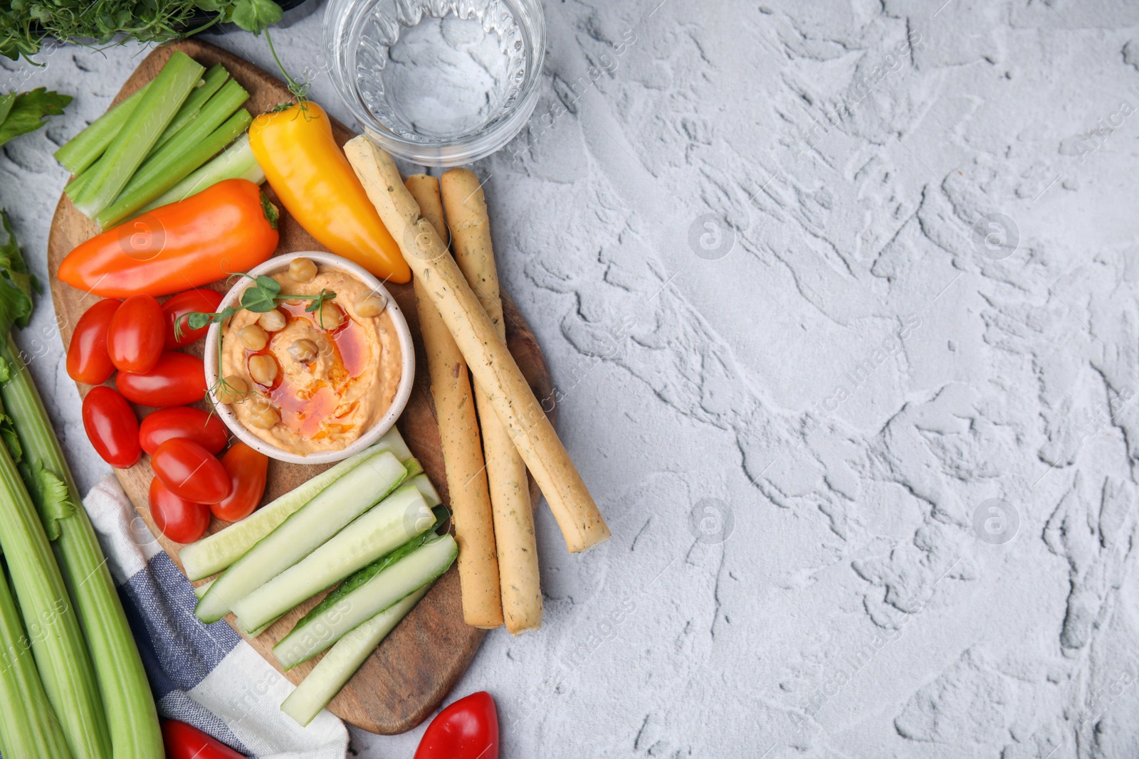 Photo of Board with delicious hummus, grissini sticks and fresh vegetables on light grey textured table, flat lay. Space for text