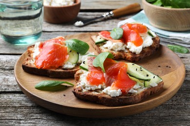 Photo of Delicious sandwiches with cream cheese, salmon, cucumber and spinach on wooden table, closeup