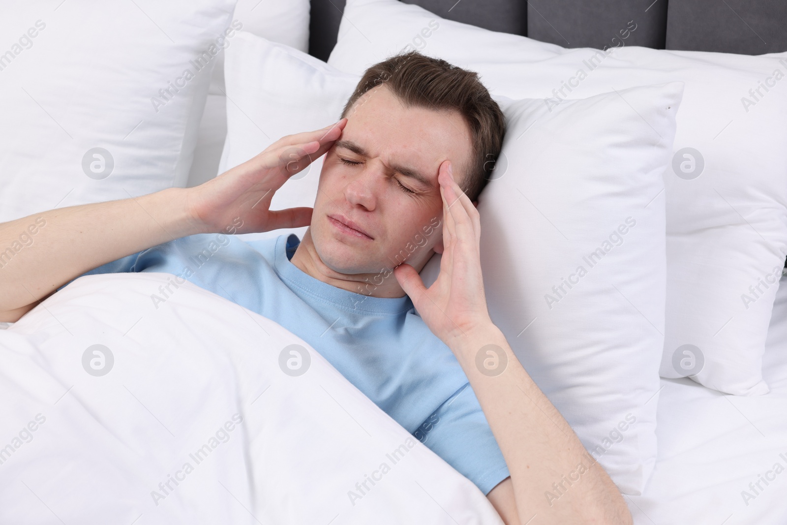 Photo of Sad man suffering from headache in bed indoors