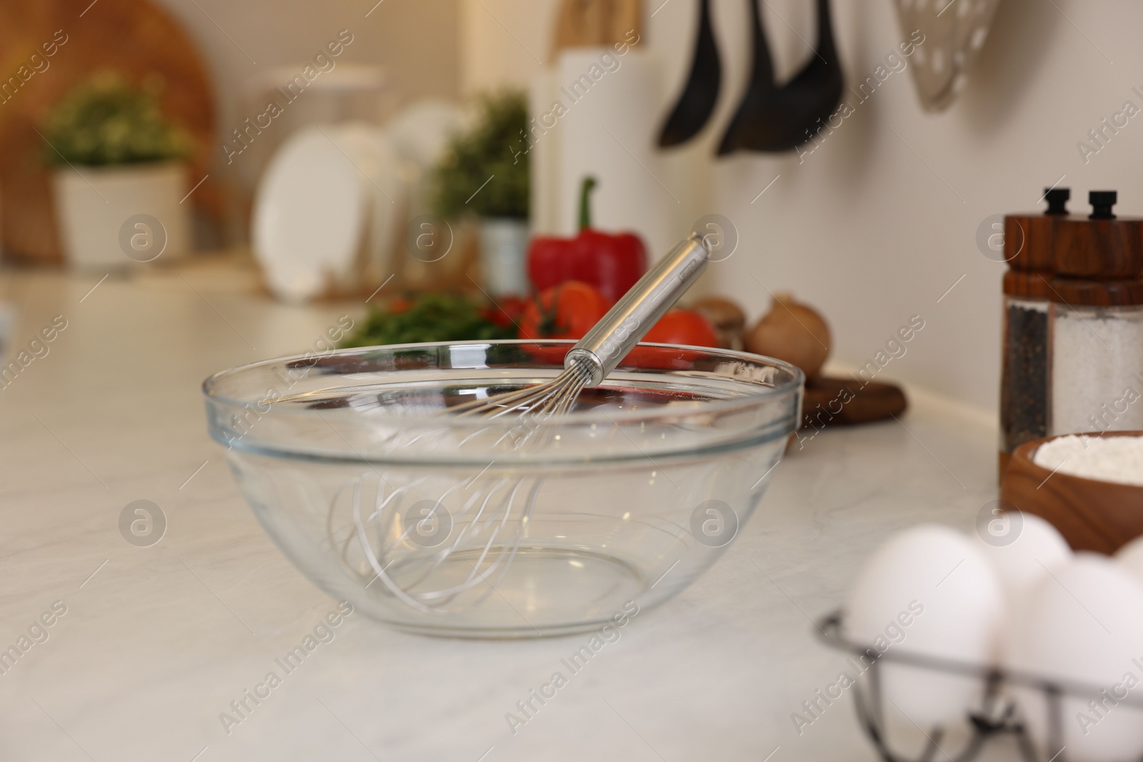 Photo of Metal whisk, bowl and different products on light table in kitchen