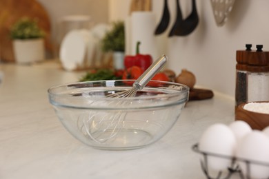 Metal whisk, bowl and different products on light table in kitchen
