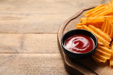 Board with tasty ketchup and ridged chips on wooden table, closeup. Space for text