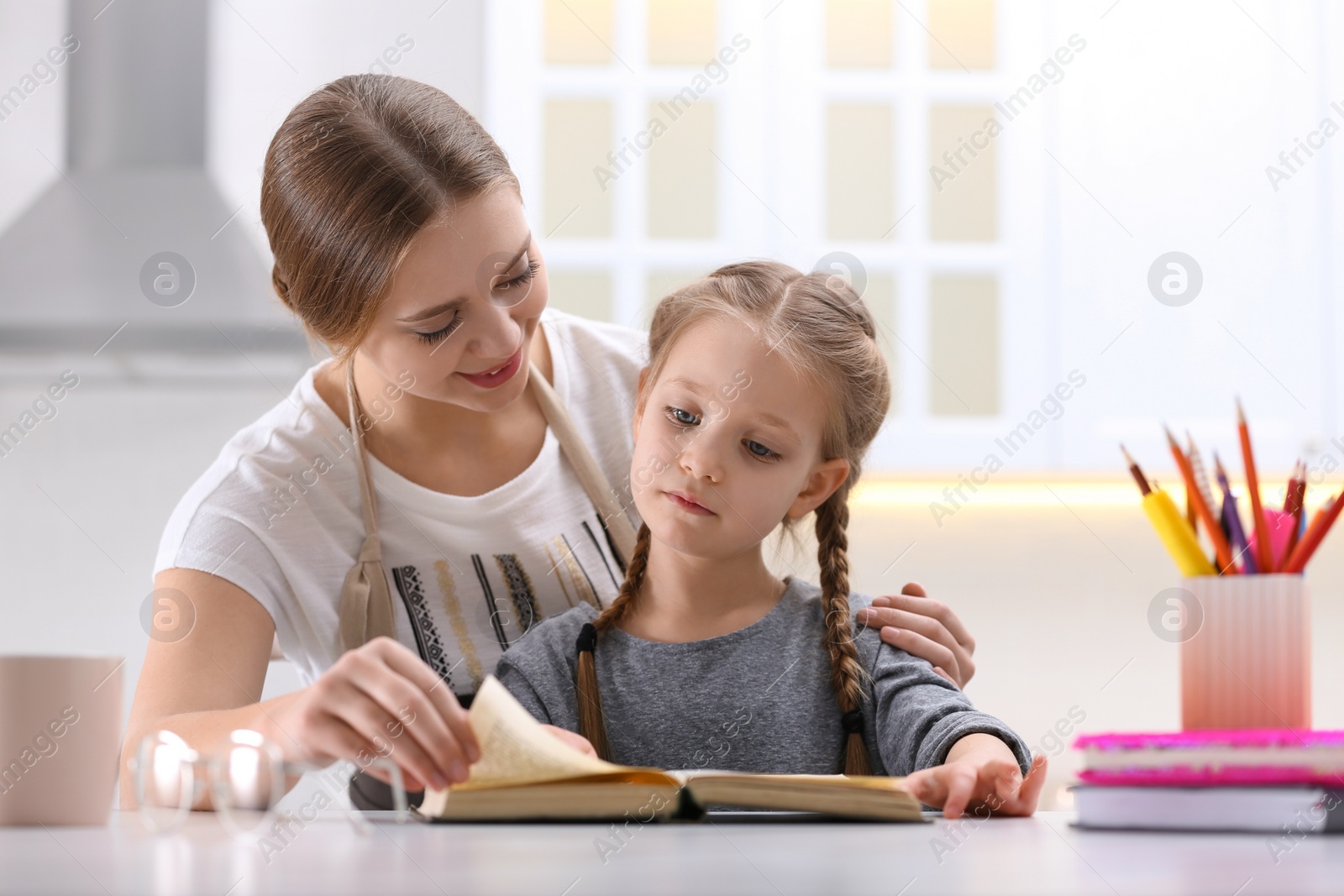 Photo of Woman helping her daughter with homework at table in kitchen