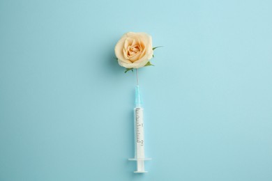 Photo of Medical syringe and beautiful rose on light blue background, top view