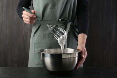 Photo of Woman making whipped cream with whisk at black table, closeup