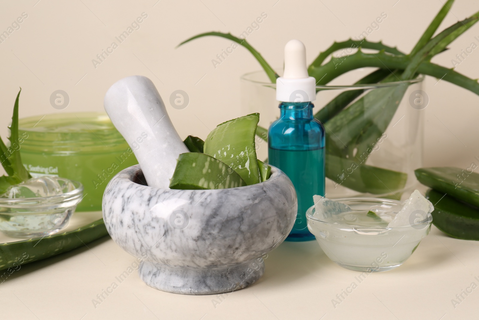 Photo of Mortar with fresh aloe and cosmetic products on beige background, closeup