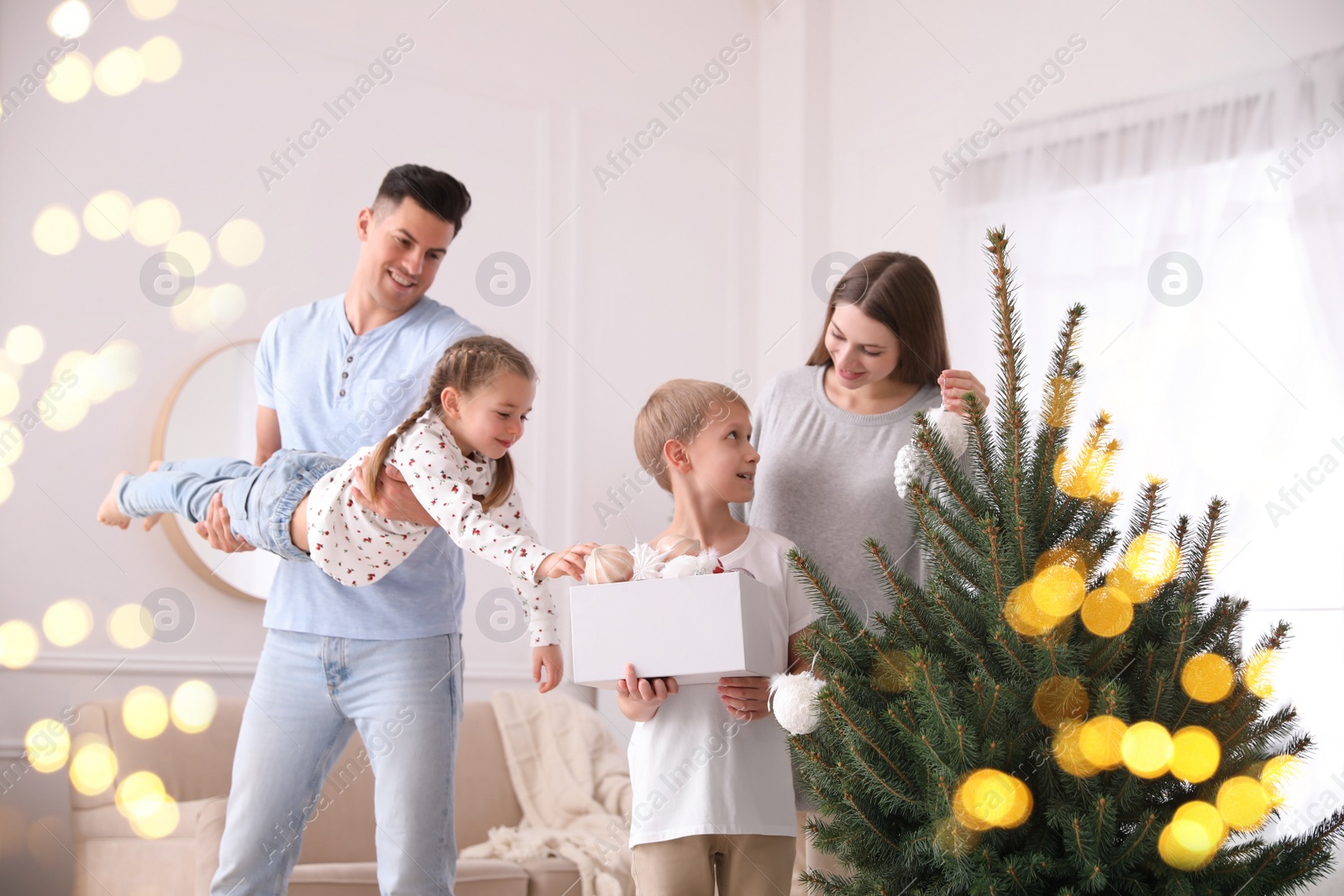 Photo of Mother and son decorating Christmas tree while father playing with daughter at home