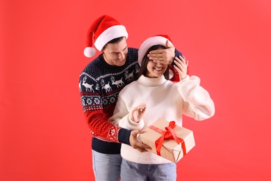 Photo of Man presenting Christmas gift to his girlfriend on red background