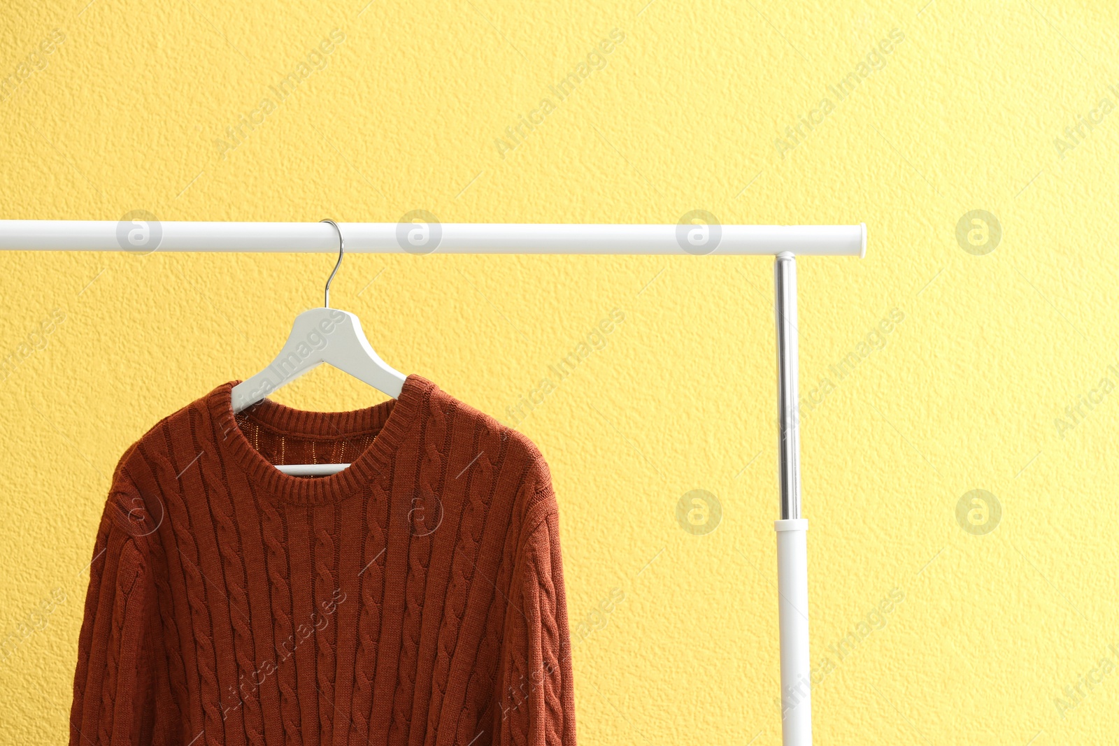 Photo of Sweater hanging on rack near yellow wall, closeup