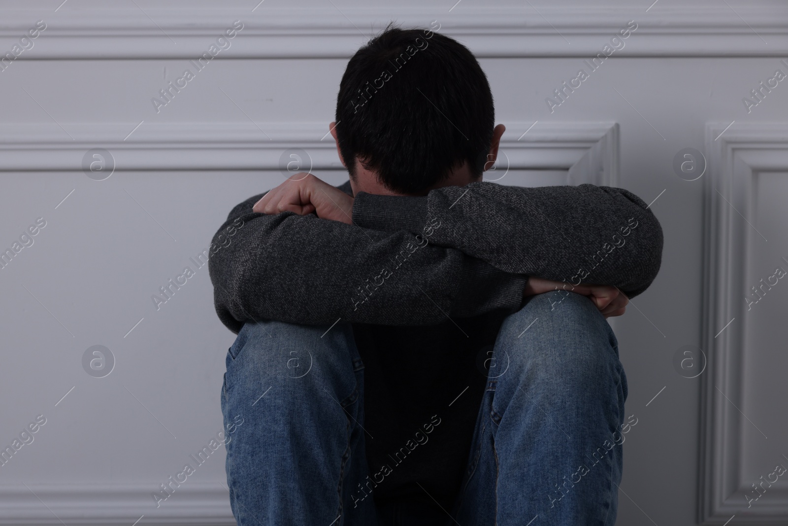 Photo of Sad man sitting near white wall indoors