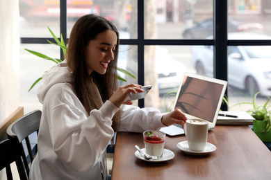 Young blogger taking picture of dessert at table in cafe