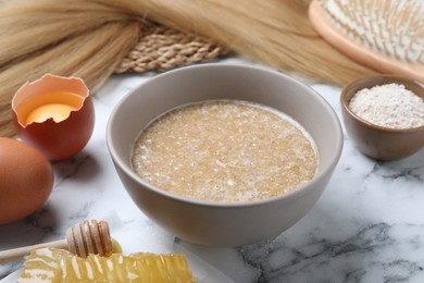 Homemade hair mask in bowl and ingredients on white marble table