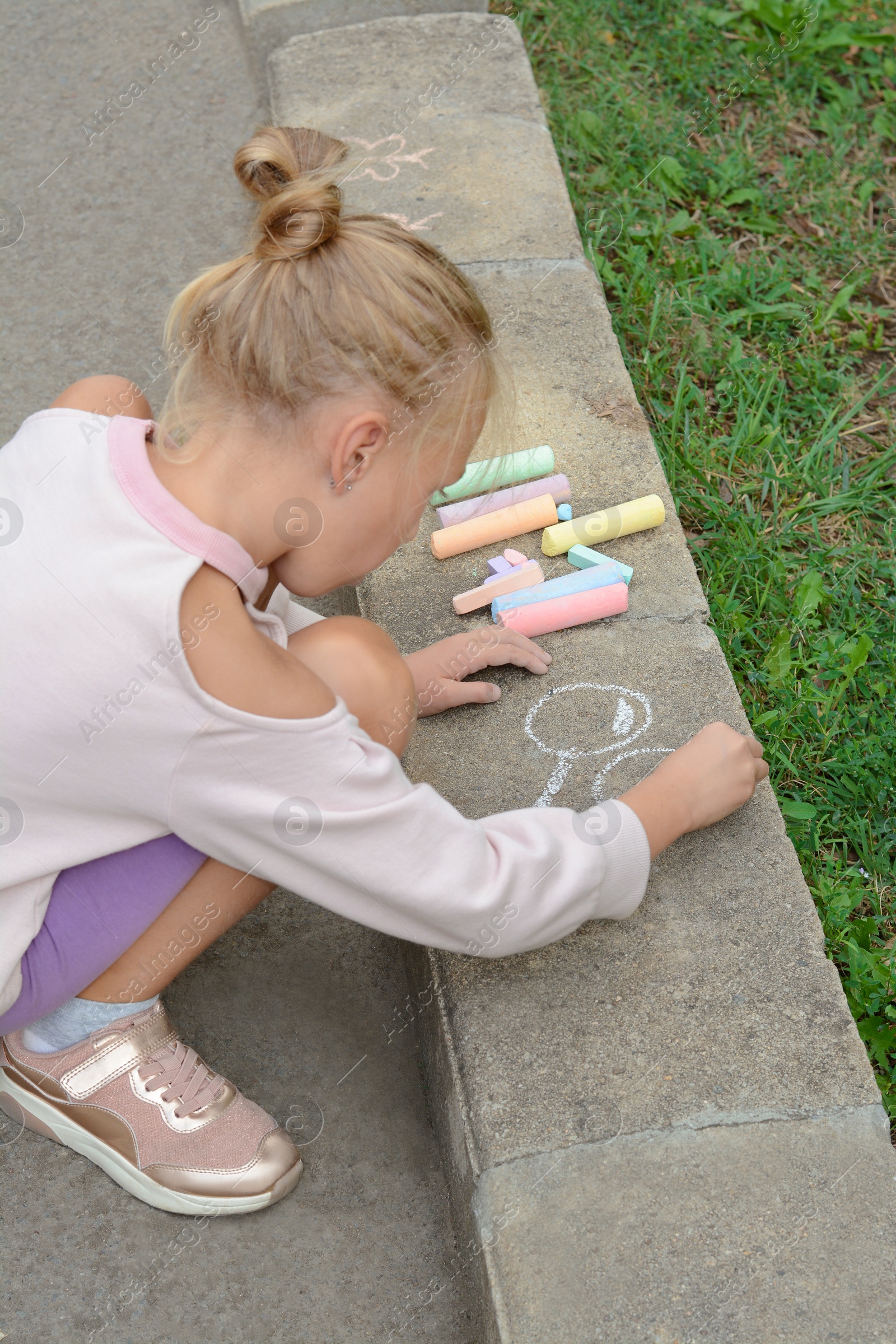 Photo of Little child drawing balloons with chalk on asphalt