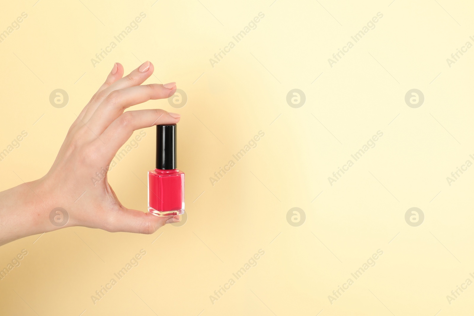 Photo of Woman holding nail polish on beige background, closeup. Space for text