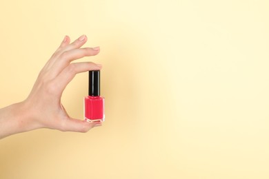 Photo of Woman holding nail polish on beige background, closeup. Space for text