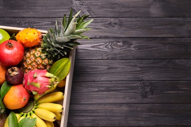 Crate with different exotic fruits on black wooden table, top view. Space for text