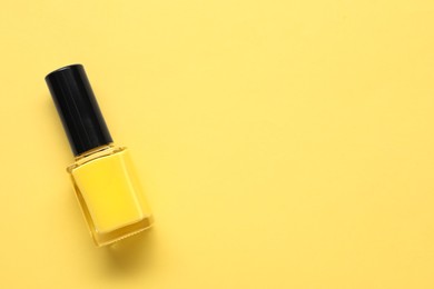Photo of Bright nail polish in bottle on yellow background, top view. Space for text