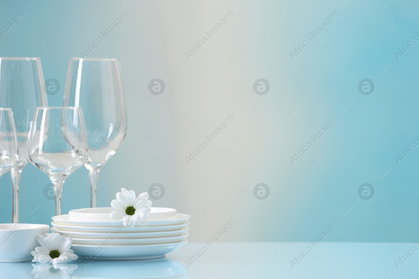 Photo of Set of many clean dishware, flowers and glasses on light blue table. Space for text