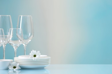 Photo of Set of many clean dishware, flowers and glasses on light blue table. Space for text