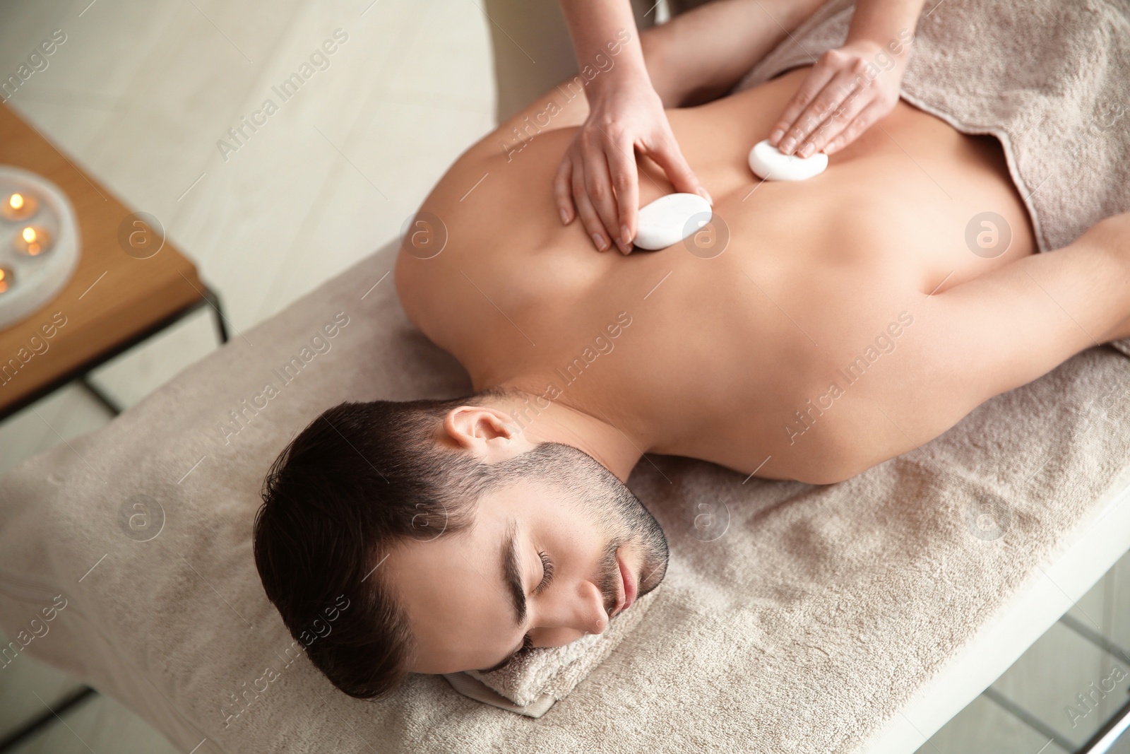 Photo of Handsome man receiving hot stone massage in spa salon, above view
