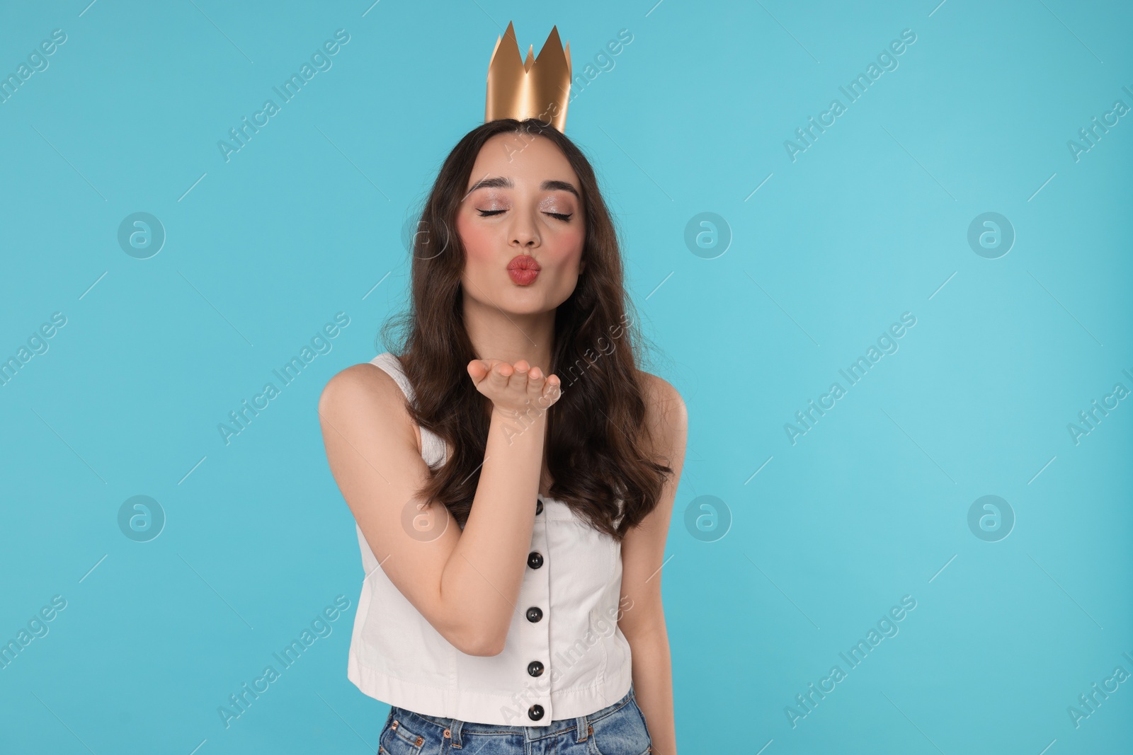 Photo of Beautiful young woman with princess crown blowing kiss on light blue background