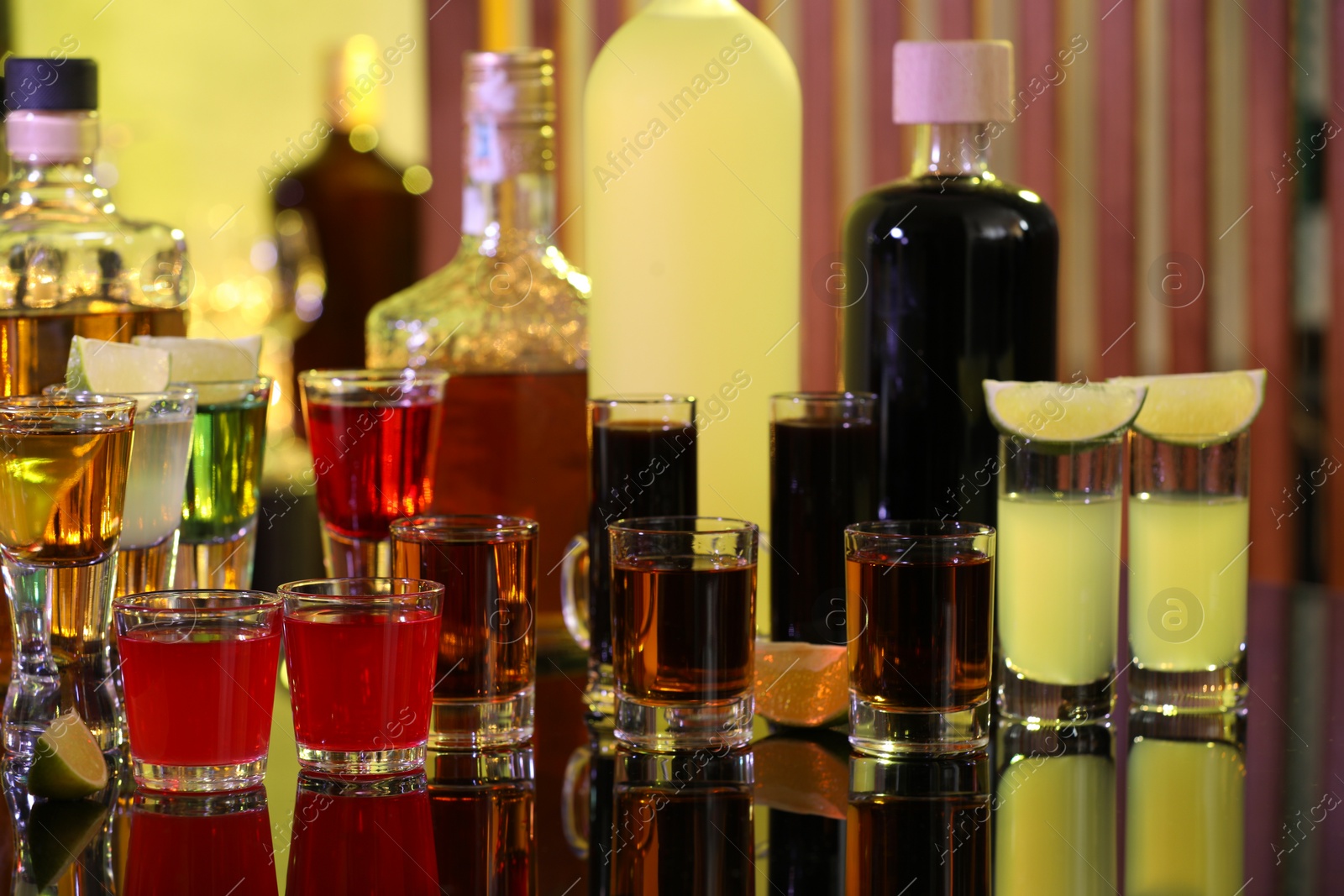 Photo of Different shooters in shot glasses and bottles on mirror surface. Alcohol drink