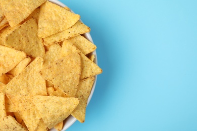 Photo of Bowl of tasty Mexican nachos chips on light blue background, top view. Space for text