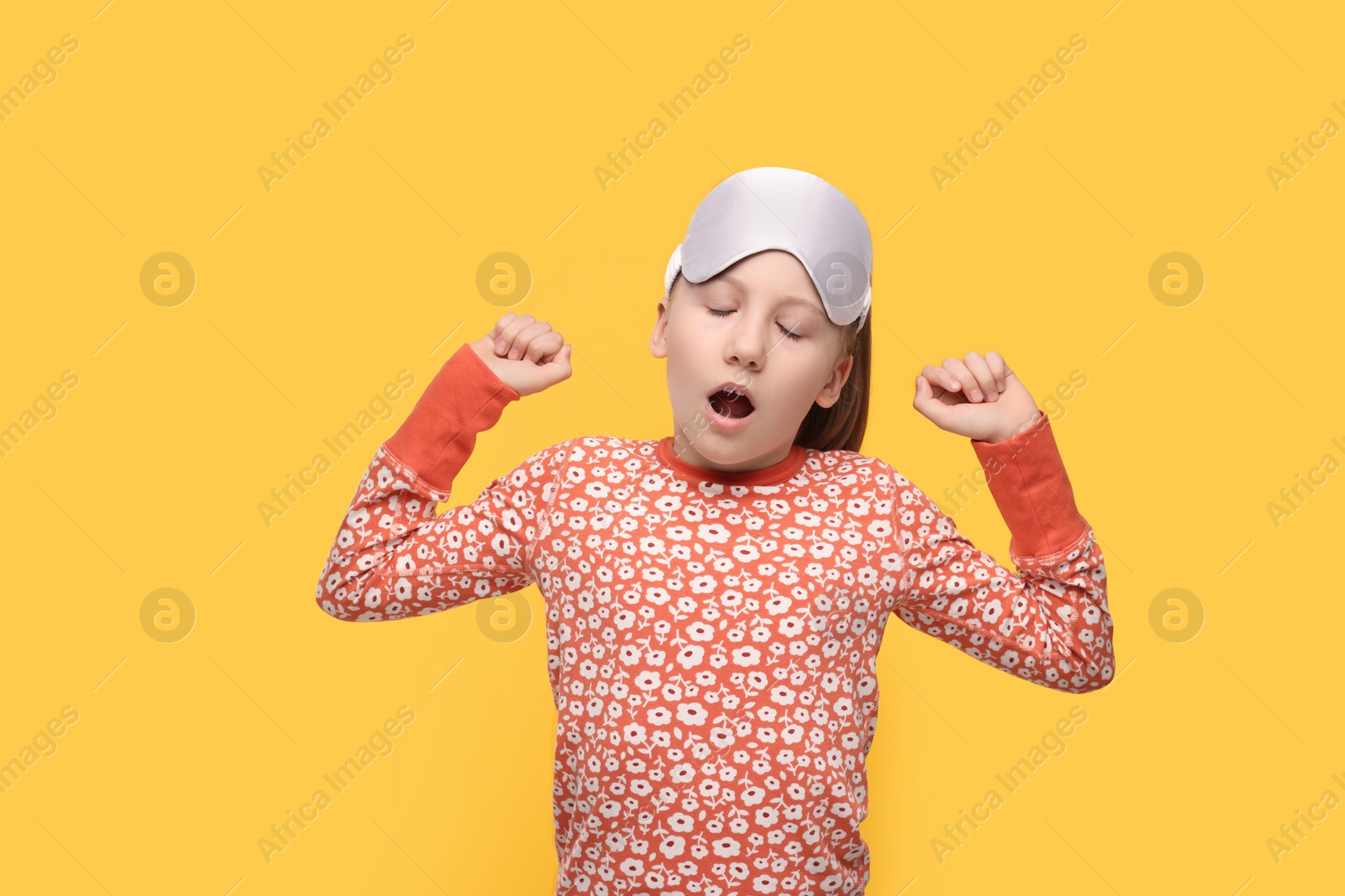 Photo of Girl with sleep mask yawning on orange background. Insomnia problem