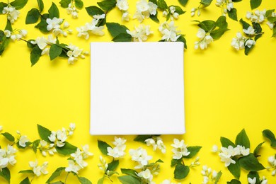 Photo of Blank canvas and beautiful jasmine flowers on yellow background, flat lay. Space for design