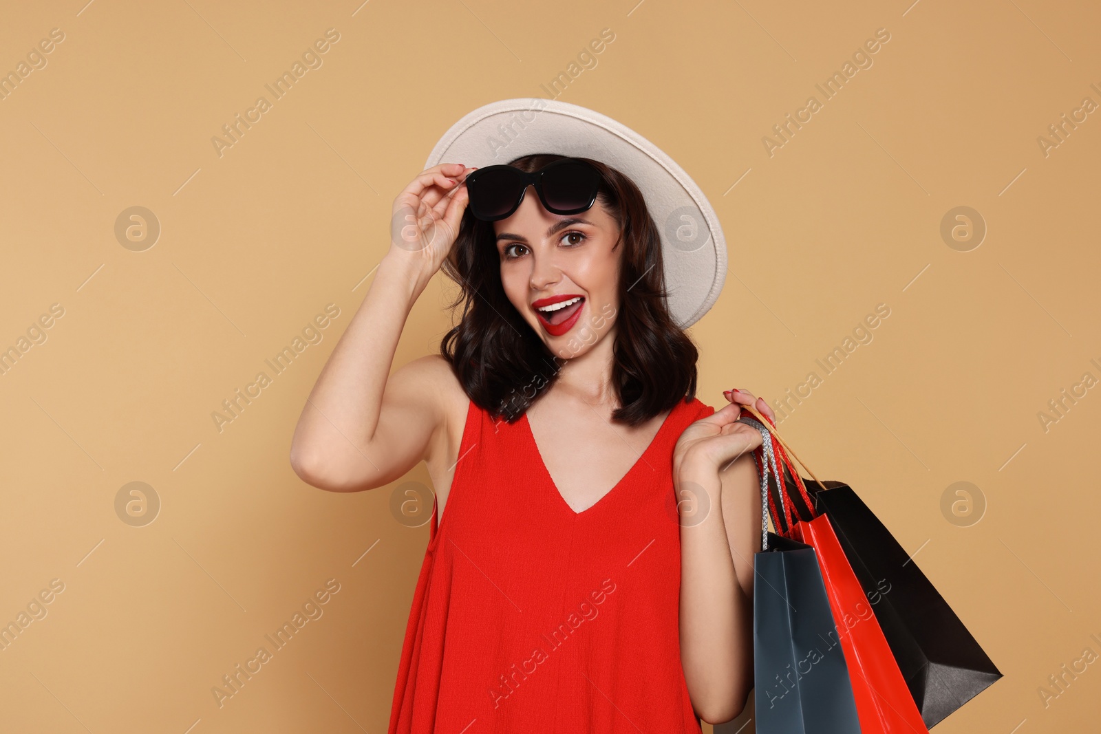 Photo of Beautiful young woman with paper shopping bags on beige background