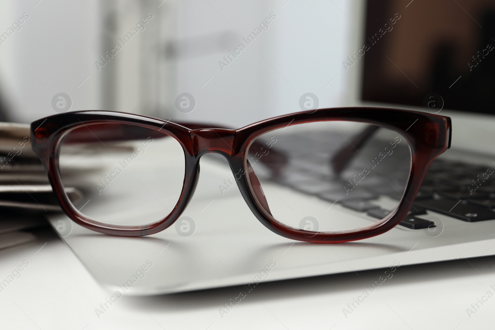 Photo of Modern laptop and glasses on white table, closeup