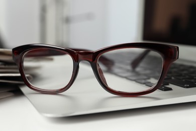 Modern laptop and glasses on white table, closeup