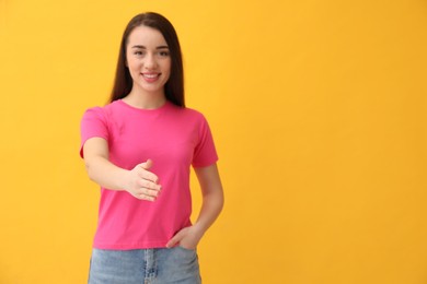 Photo of Happy young woman offering handshake against yellow background, focus on hand. Space for text