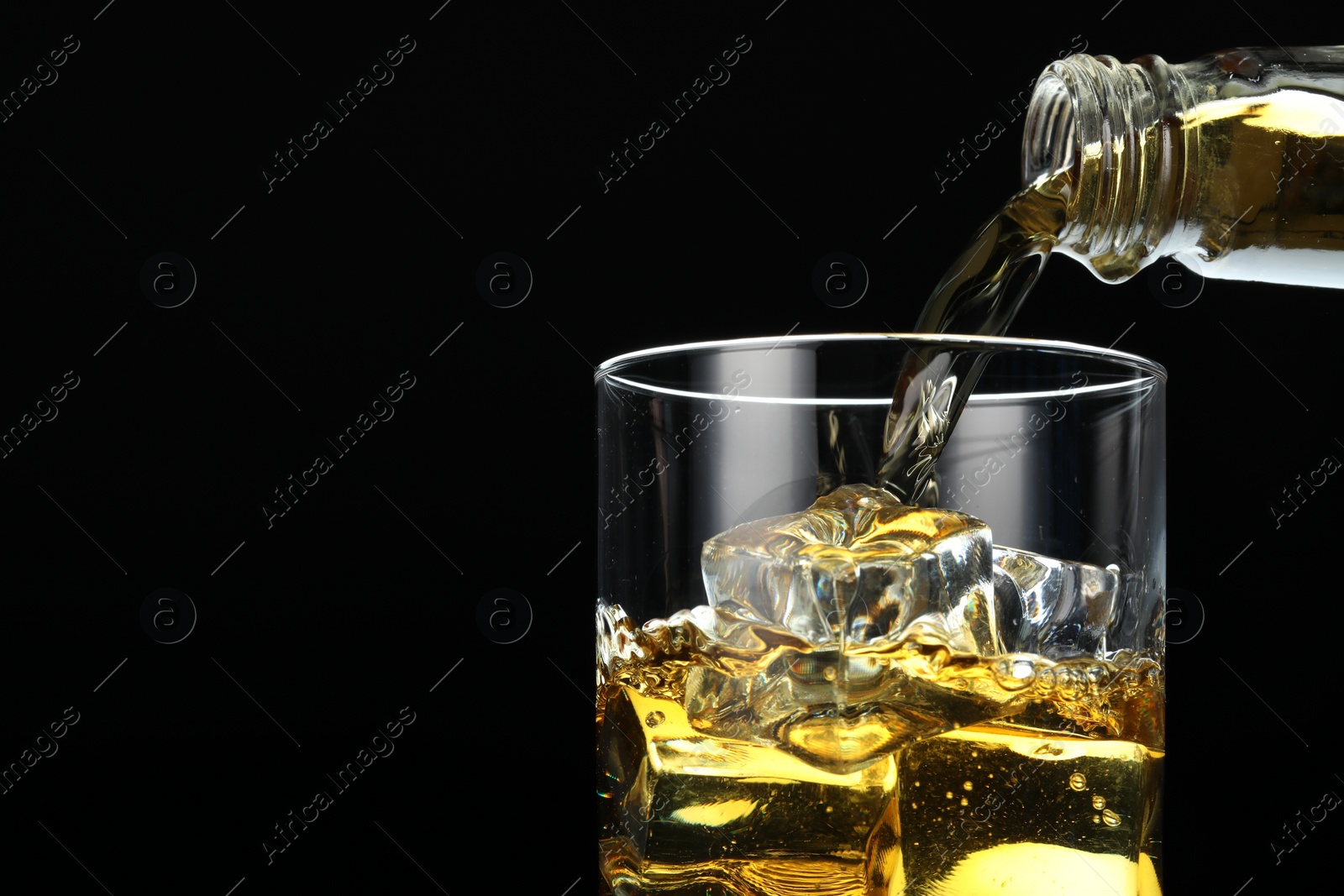 Photo of Pouring whiskey into glass with ice cubes on black background, closeup. Space for text