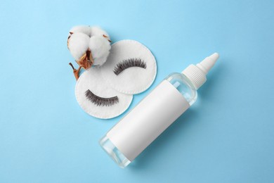 Bottle of makeup remover, cotton flower, pads and false eyelashes on light blue background, flat lay