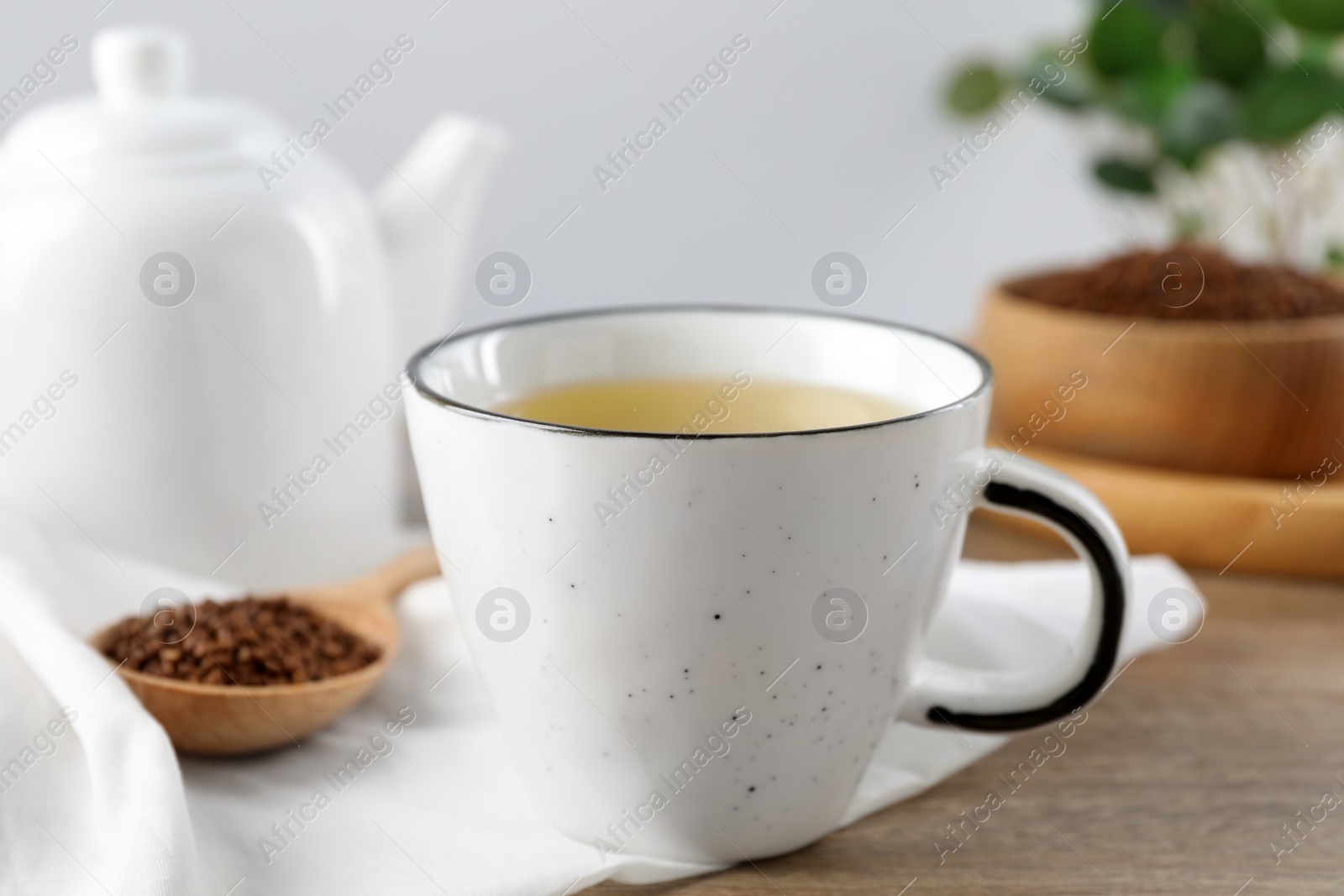 Photo of Buckwheat tea in cup and spoon with granules on wooden table, closeup