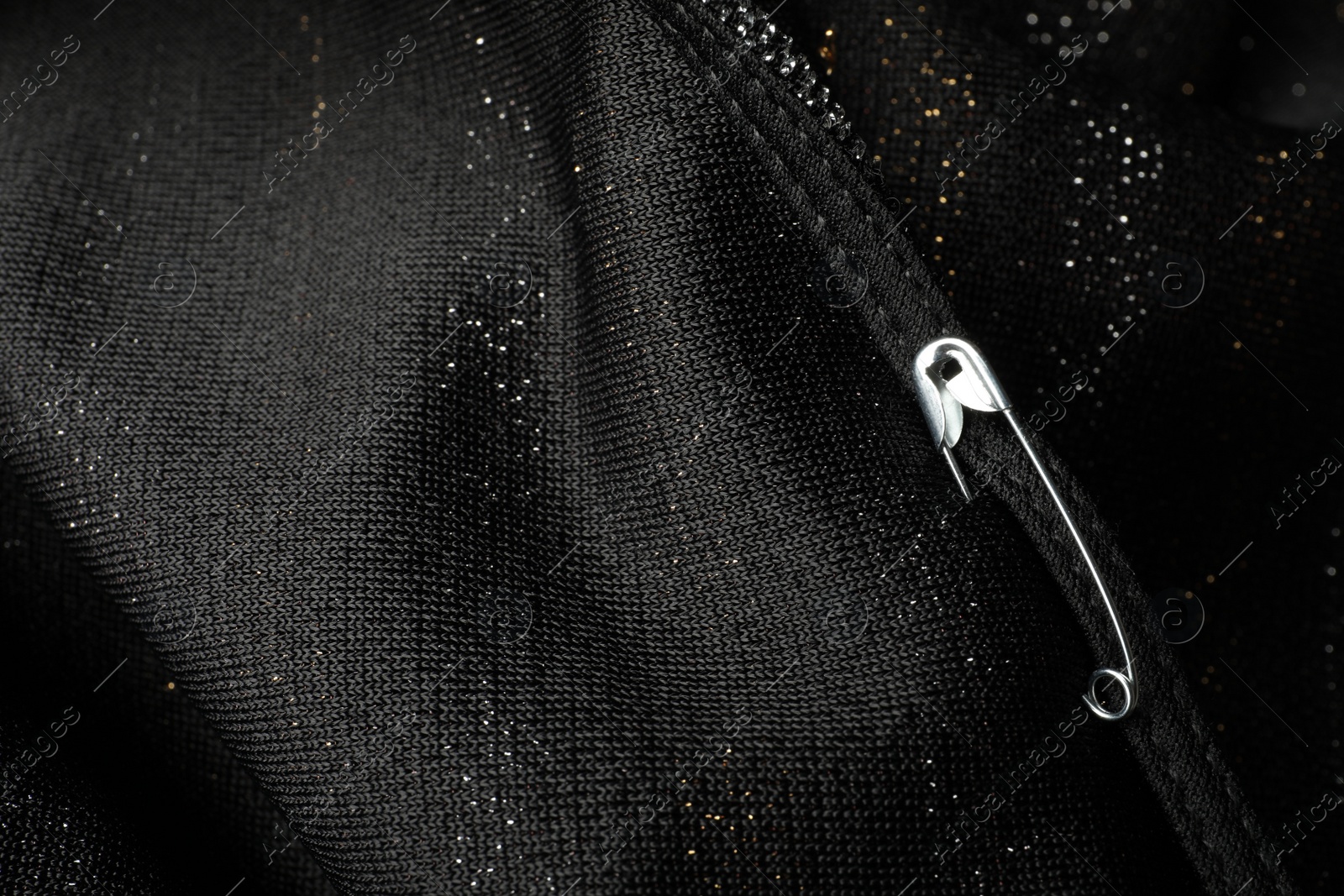 Photo of Metal safety pin on black fabric, closeup