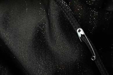 Metal safety pin on black fabric, closeup