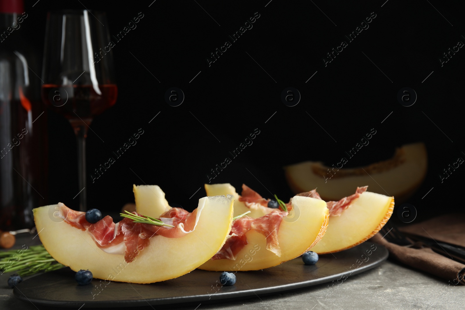 Photo of Melon with prosciutto, blueberries and rosemary on table