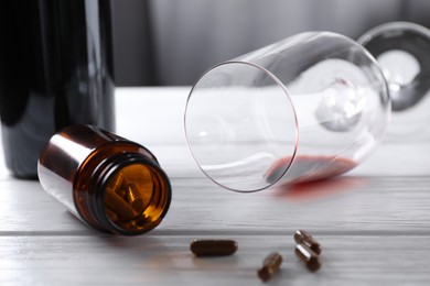 Photo of Alcohol and drug addiction. Overturned glass with red wine, bottle and pills on white wooden table, closeup