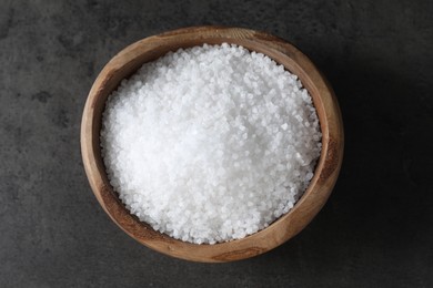 Photo of Natural salt in wooden bowl on dark grey table, top view