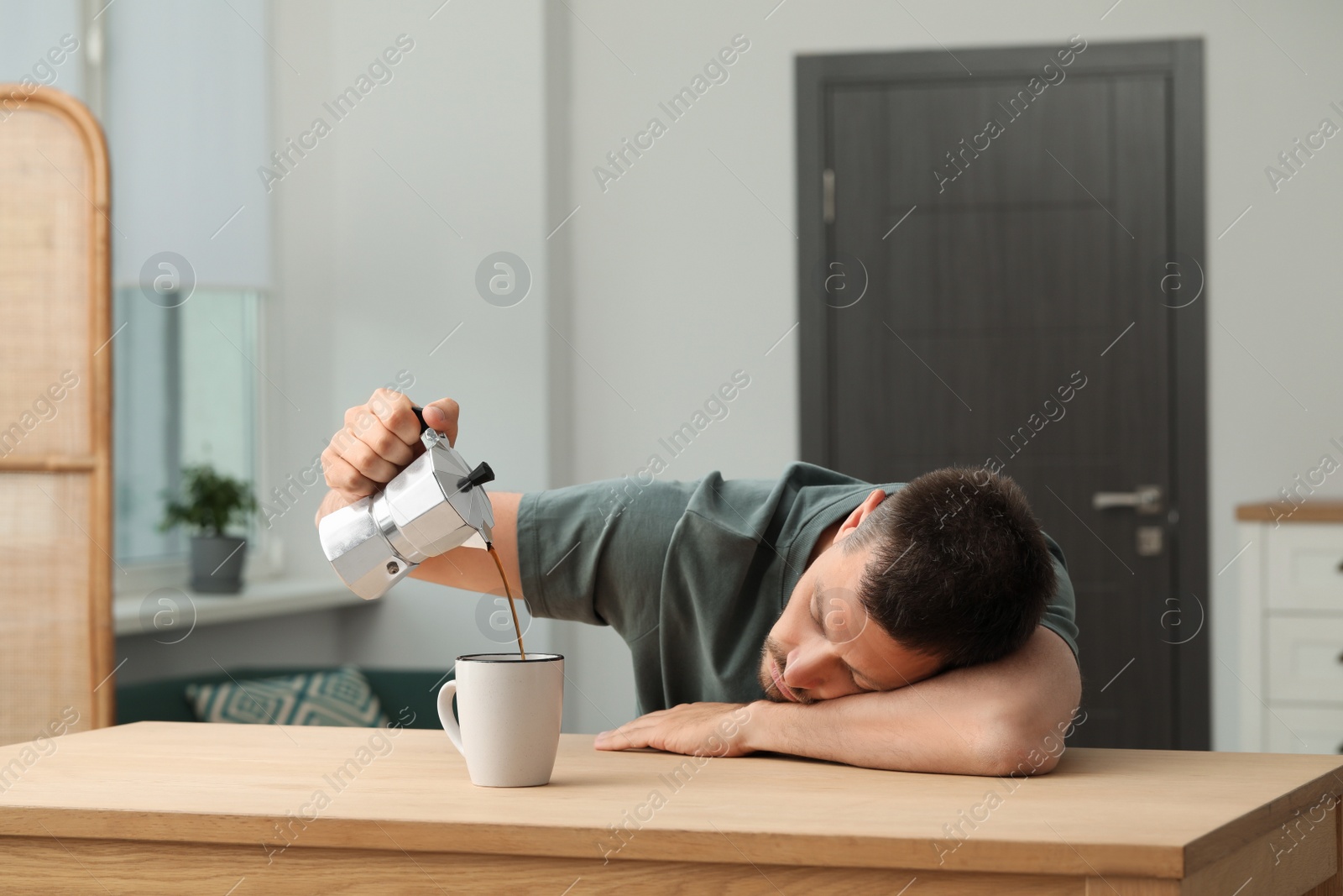 Photo of Sleepy man pouring coffee in cup at wooden table indoors