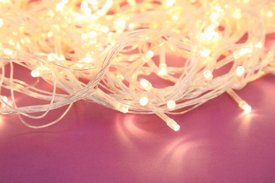 Photo of Glowing Christmas lights on color background, closeup