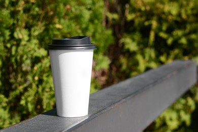 Photo of Takeaway coffee cup on metal railing outdoors. Space for text